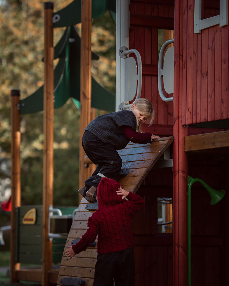 A girl is climbing up on a climbing wall to a playground unit platform.